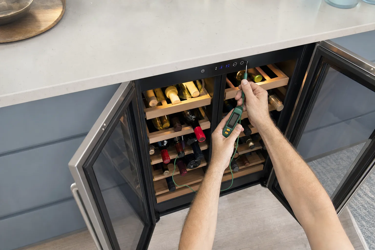 Overhead view of an open undercounter wine cooler, a probe thermometer held over the loaded wine racks
